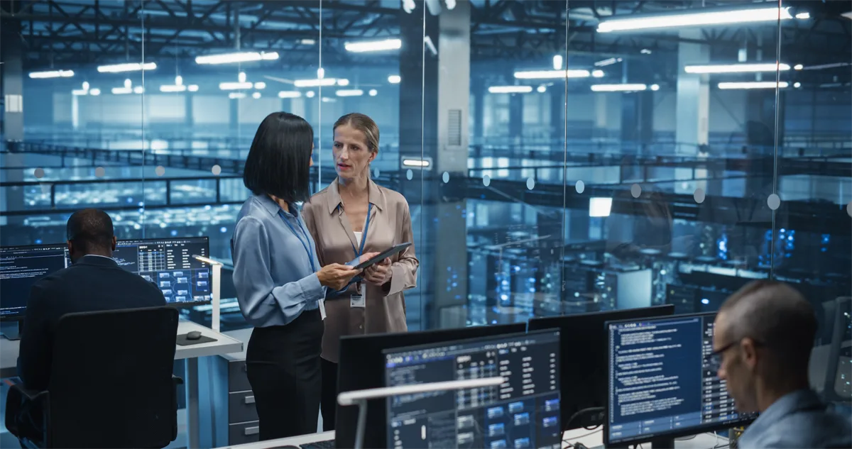 In a modern data center, a data scientist and AI specialist analyze algorithms on a tablet computer.