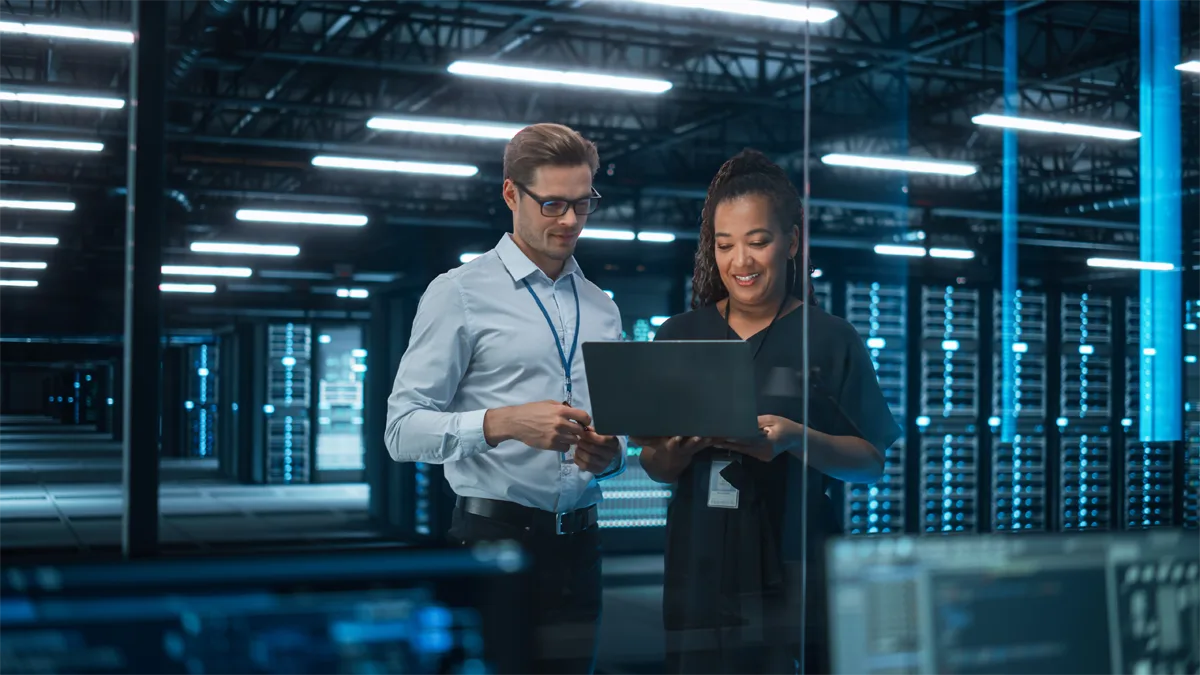 Two IT professionals reviewing a laptop in a data center